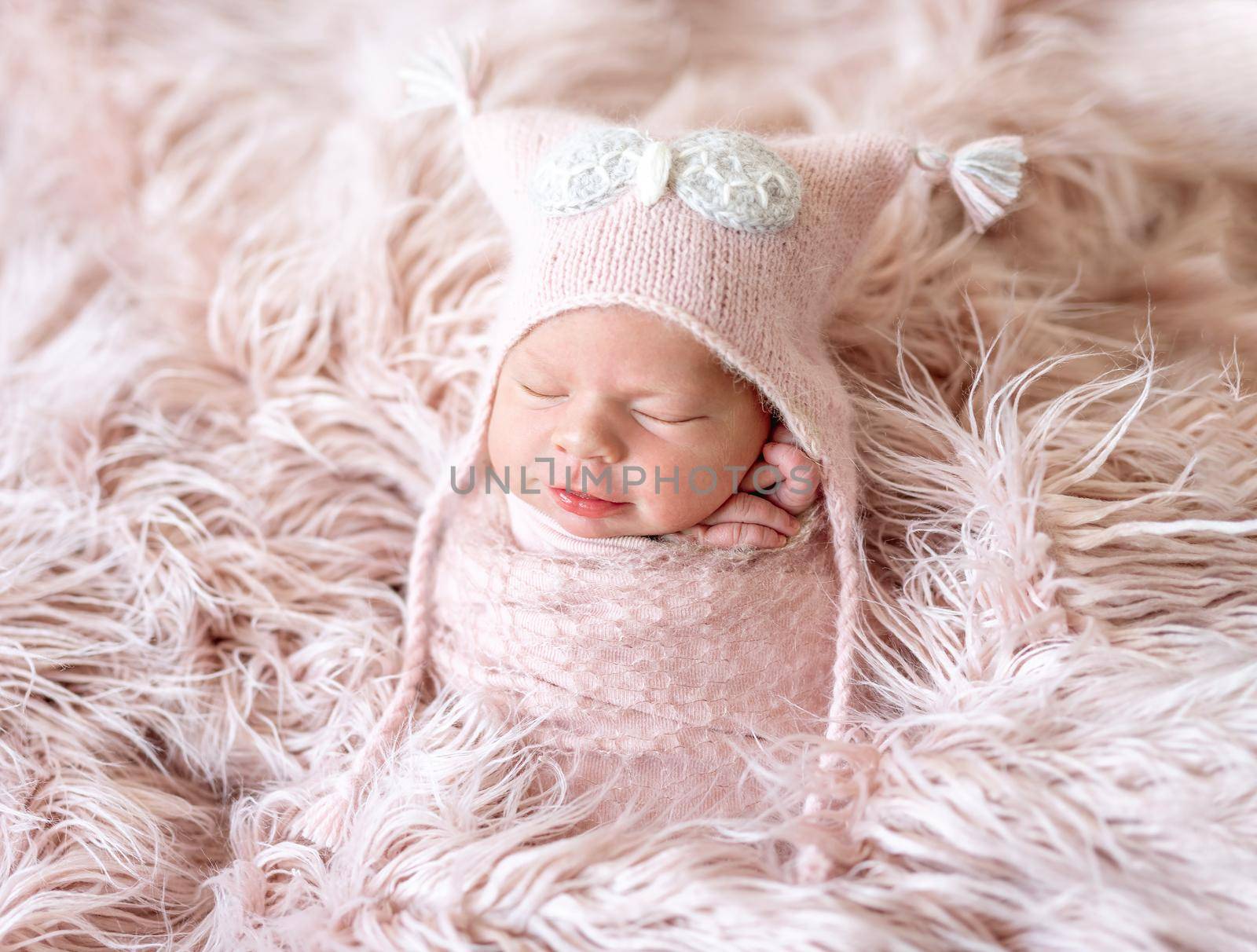 New born child asleep wrapped in soft pink blanket, on bed