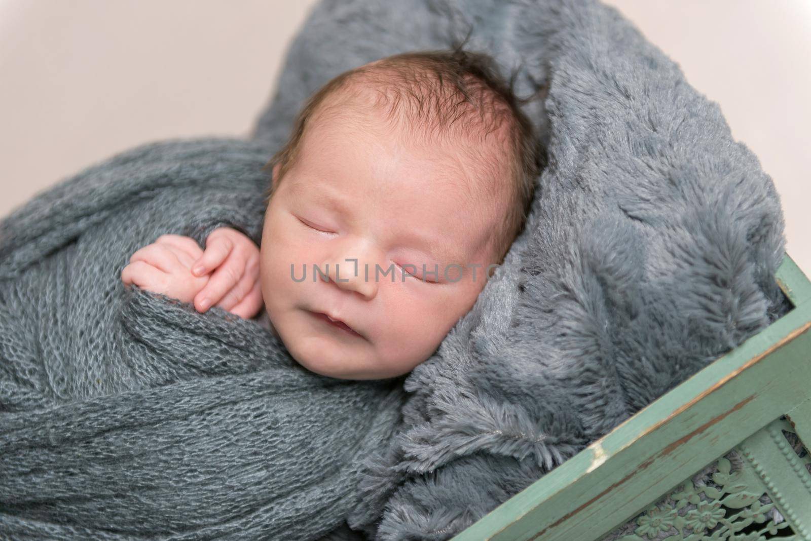 Adorable hairy infant sleeping tight in a basket, all covered with dark gray wrapping, closeup