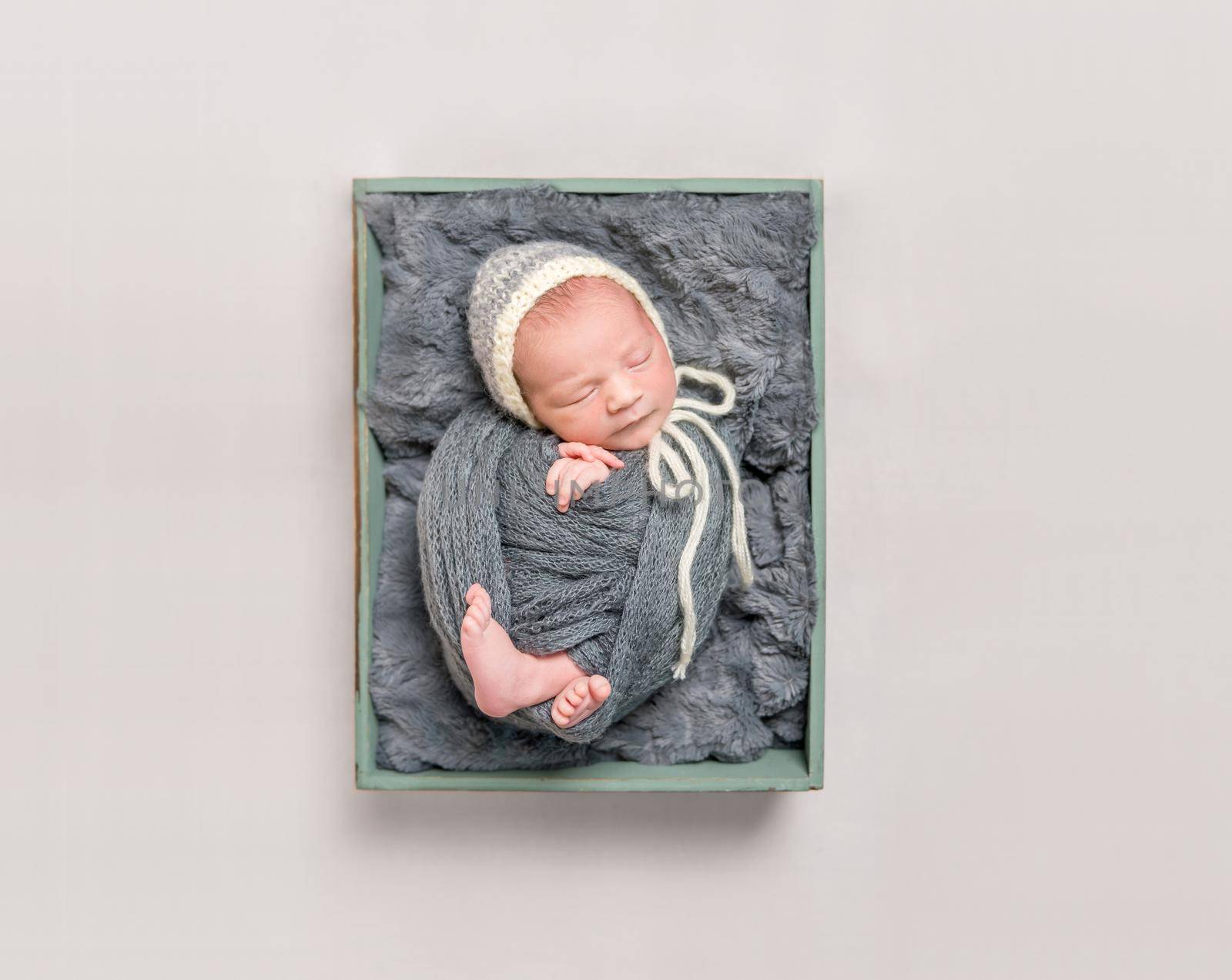 Sweet baby wrapped in a dark gray blanket resting in child's basket, topshot