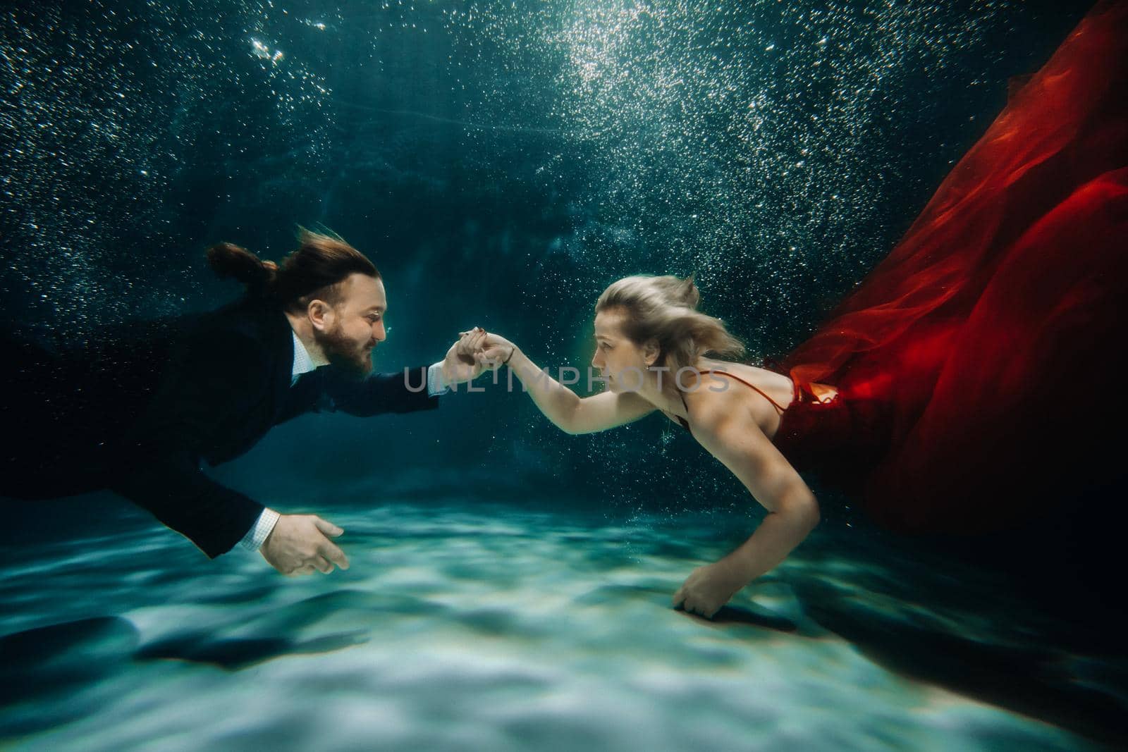 A woman in a red dress and a man in a suit meet under water.A couple of lovers under the water by Lobachad