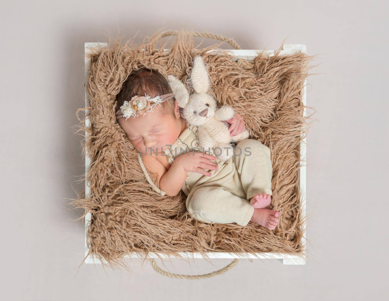 Adorable child napping on her back with a lovely rabbit toy, in a basket, topview
