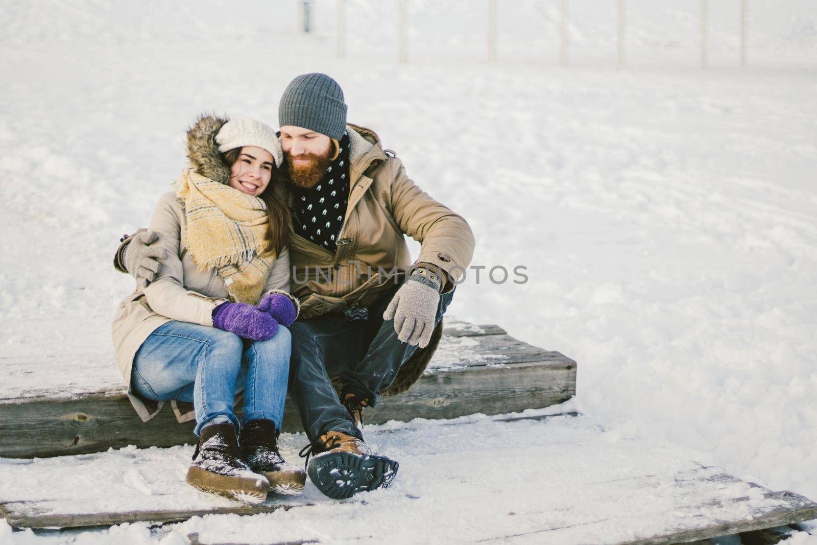 Loving couple young people a man with a beard and a Caucasian woman are sitting on a wooden staircase in the winter on the snow St. Valentine's Day a date Christmas hugging and happy.