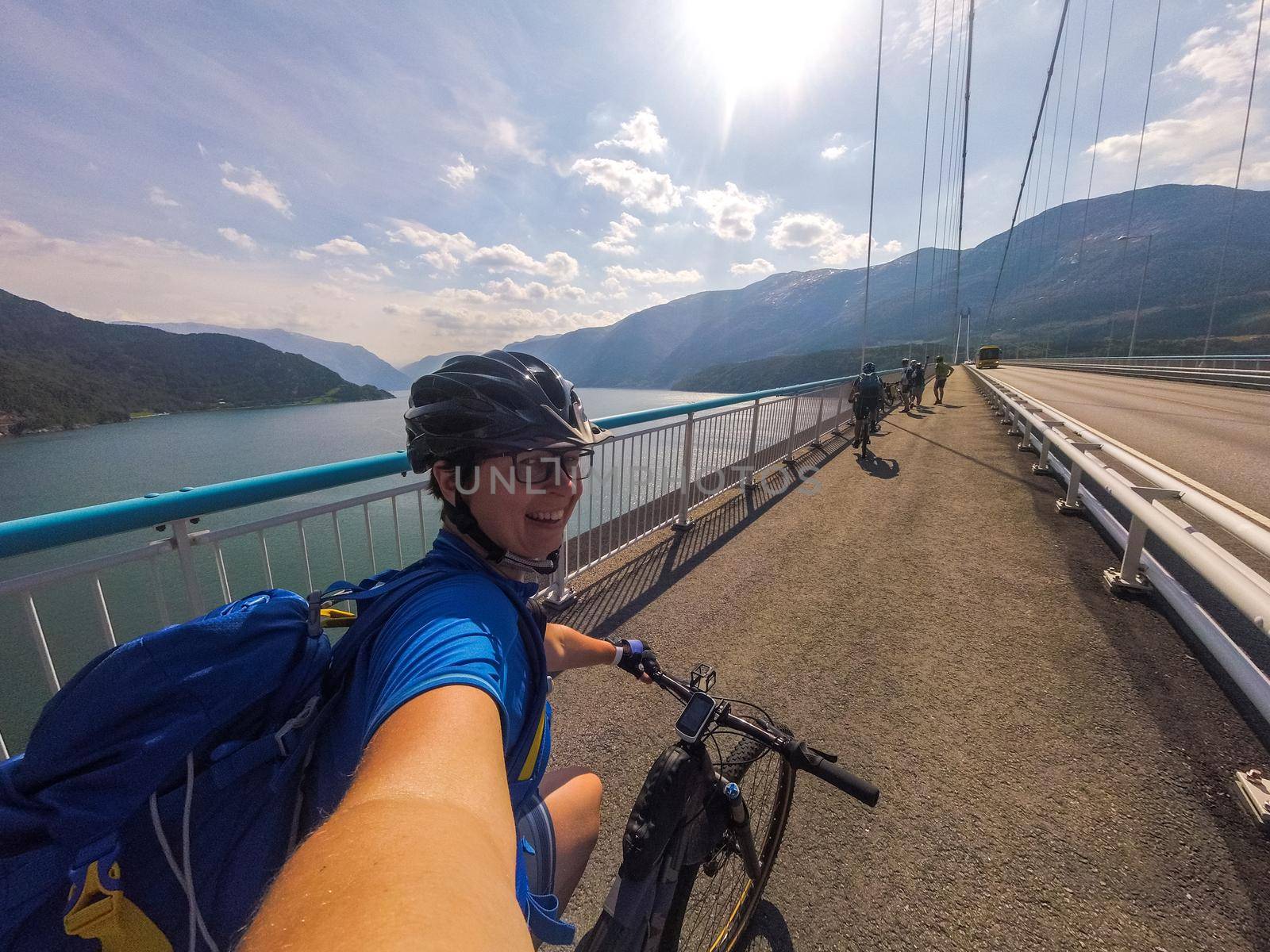 Theme of mountain biking in Scandinavia. human tourist in helmet and sportswear on bicycle in Norway on Hardanger Bridge suspension bridge thrown across the Hardanger Fjord in southwestern Norway by Tomashevska