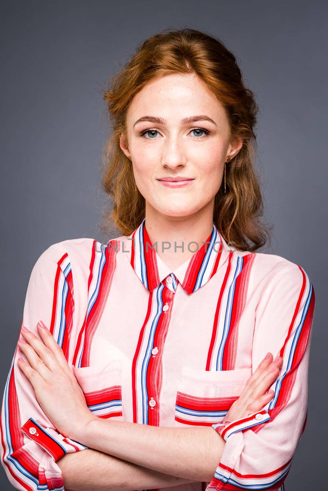 portrait of a young red-haired beautiful girl in the studio on a gray isolated background. A woman stands and smiles in a red shirt with a short sleeve. Business concept by Tomashevska