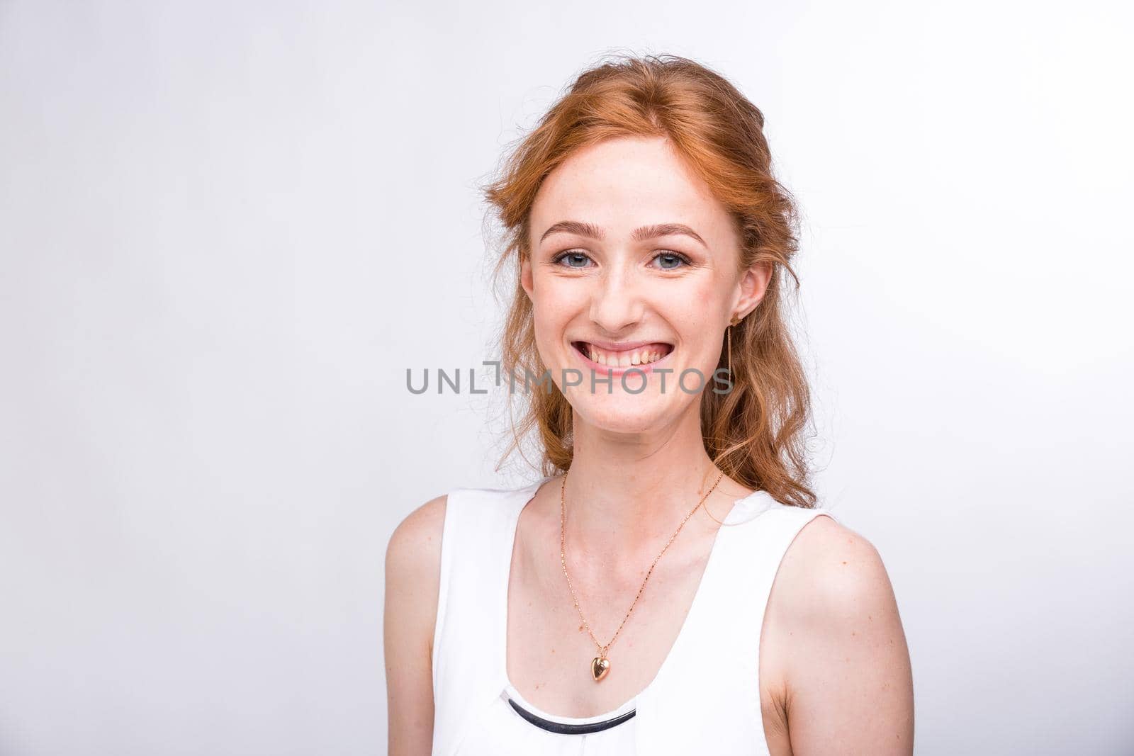 Portrait of a beautiful young female student with a smile in a white shirt of European, Caucasian nationality with long red hair and freckles on her face posing on a white background in the studio.