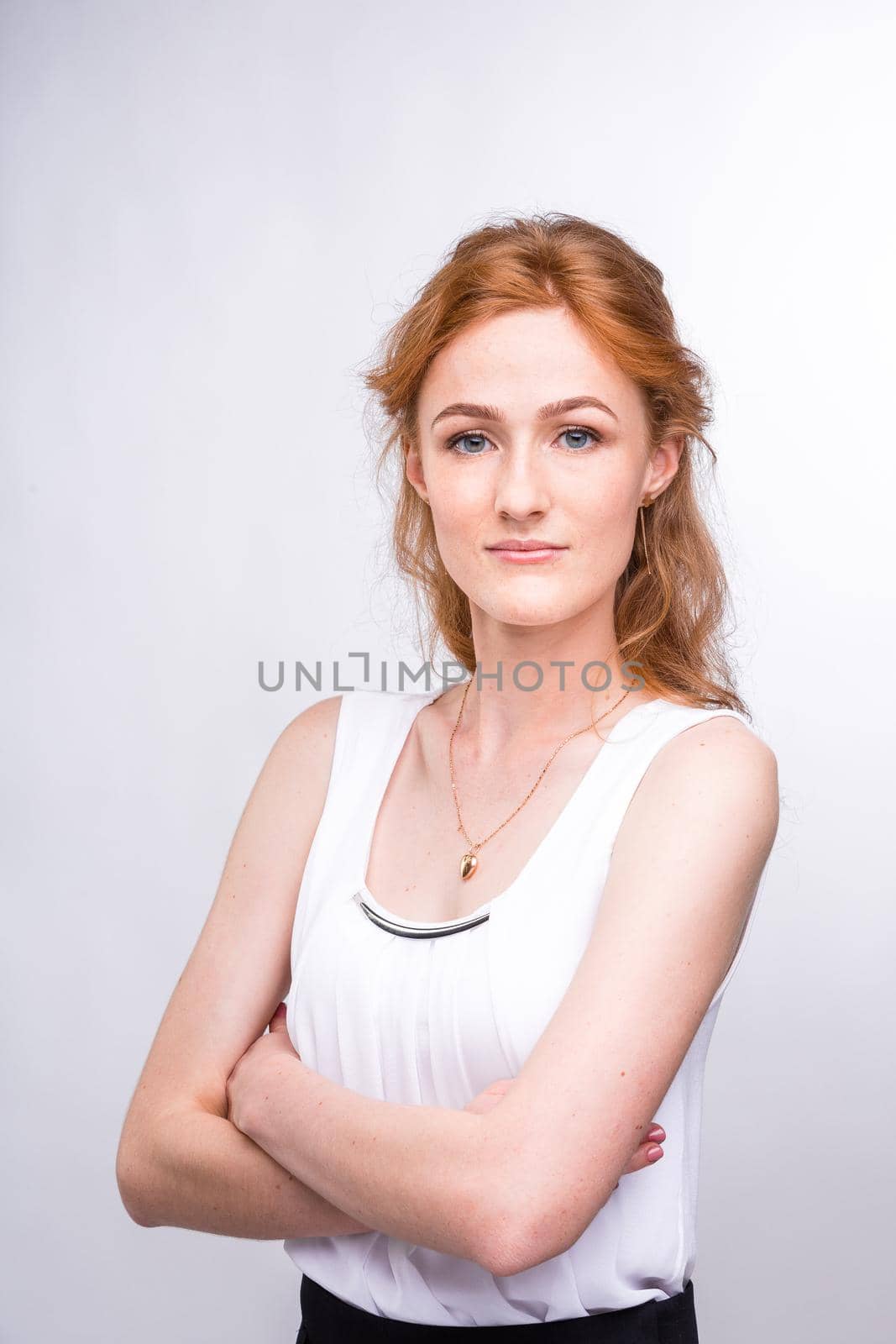 Portrait of a beautiful young woman of European, Caucasian nationality with long red hair and freckles on her face posing on a white background in the studio. Close-up student girl in a white blouse.