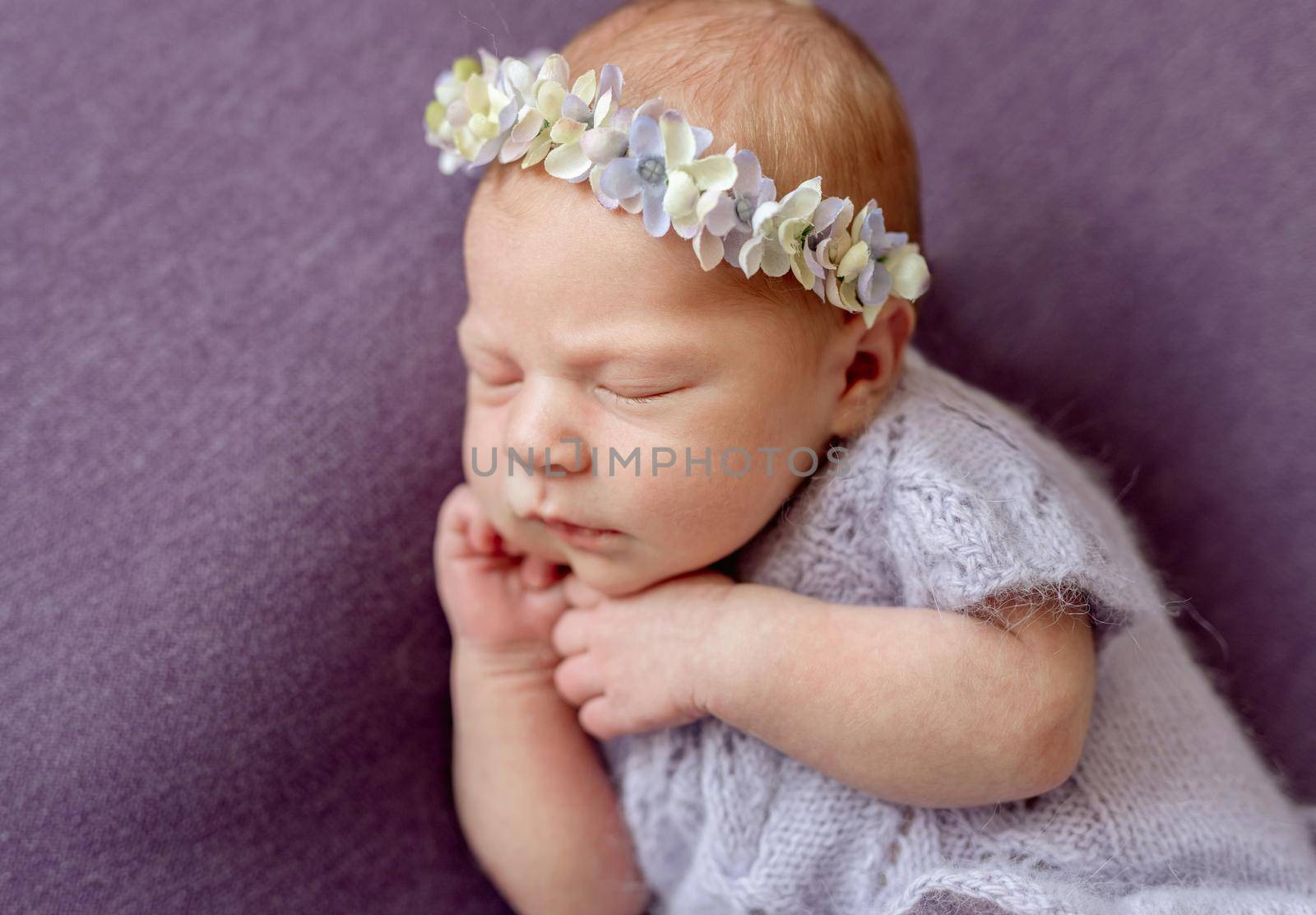 Quiet newborn in cute knitted violet blue wool jacket and floral headband