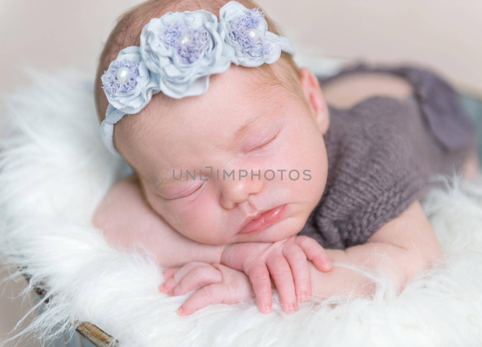 Amazing infant girl with flowery hairband sleeping wearing brown cute suit, on a soft pillow