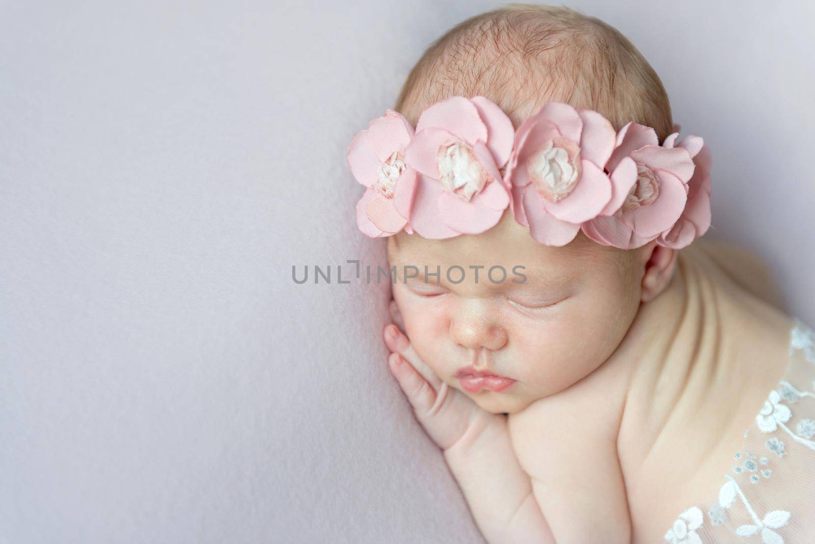 Sweet little girl with massive pink flowers on her head napping on her belly