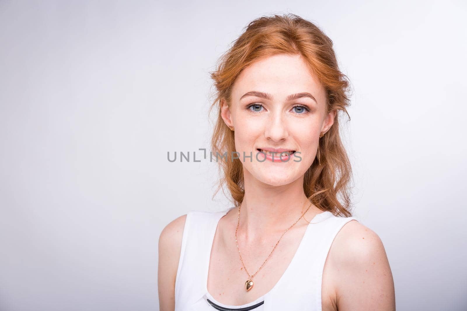 Portrait of a beautiful young female student with a smile in a white shirt of European, Caucasian nationality with long red hair and freckles on her face posing on a white background in the studio.