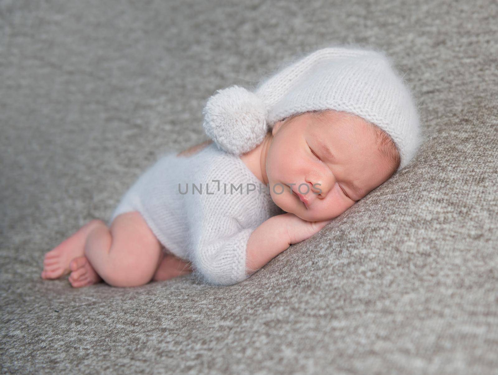 Sweet little baby boy in light blue costume and knitted bonnet with pom pom on grey background.