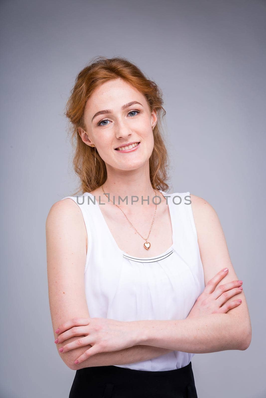 portrait vertical up to the waist young, beautiful business woman, student with lred, curly hair and freckles on gray background. SHe dressed in a white blouse with short sleeves about open shoulders by Tomashevska