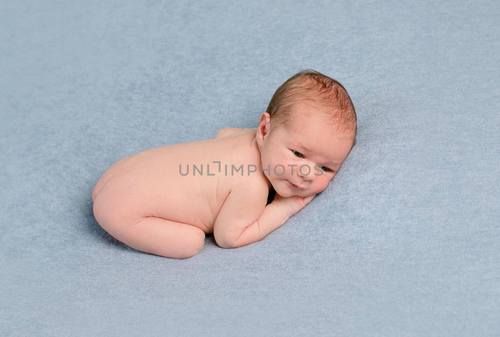 Adorable newborn baby in embryo pose lies on grey blanket.