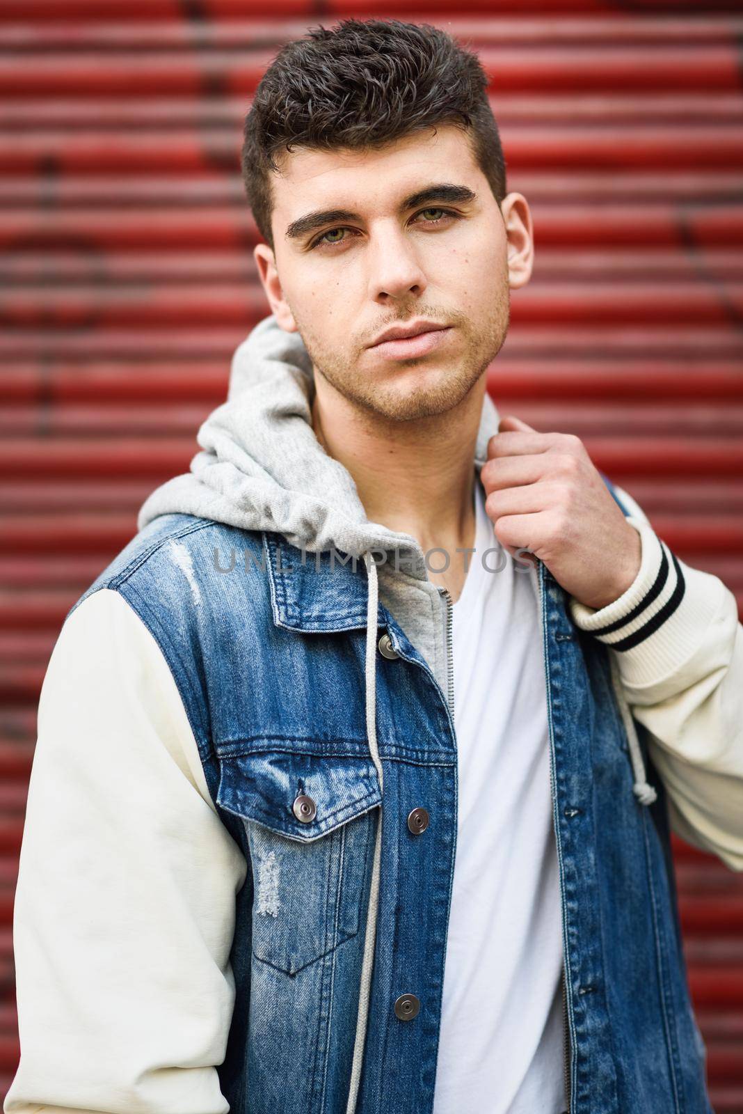 Good looking young man with blue eyes in the street. Model of fashion in urban background wearing white t-shirt, jeans and blue jacket