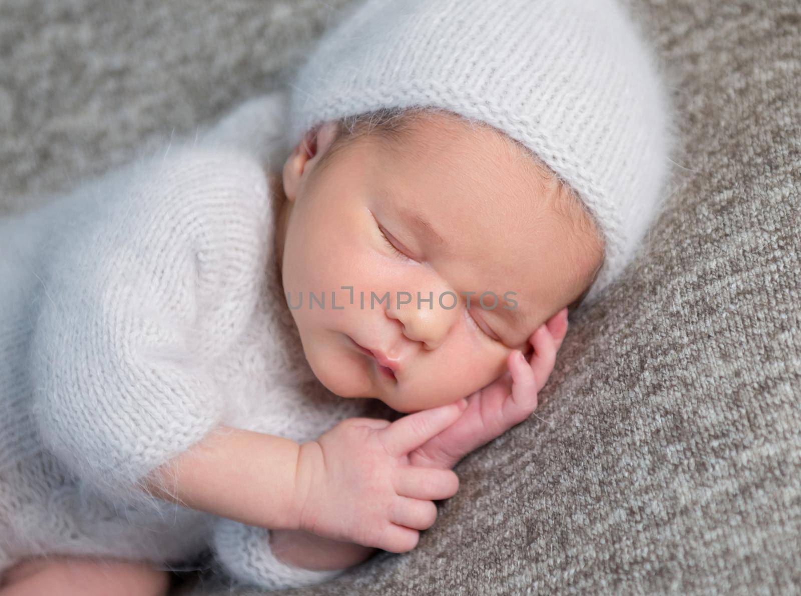 Portrait of newborn baby boy sleeping happily and holding his small handsunder his head. Close-up, grey background.