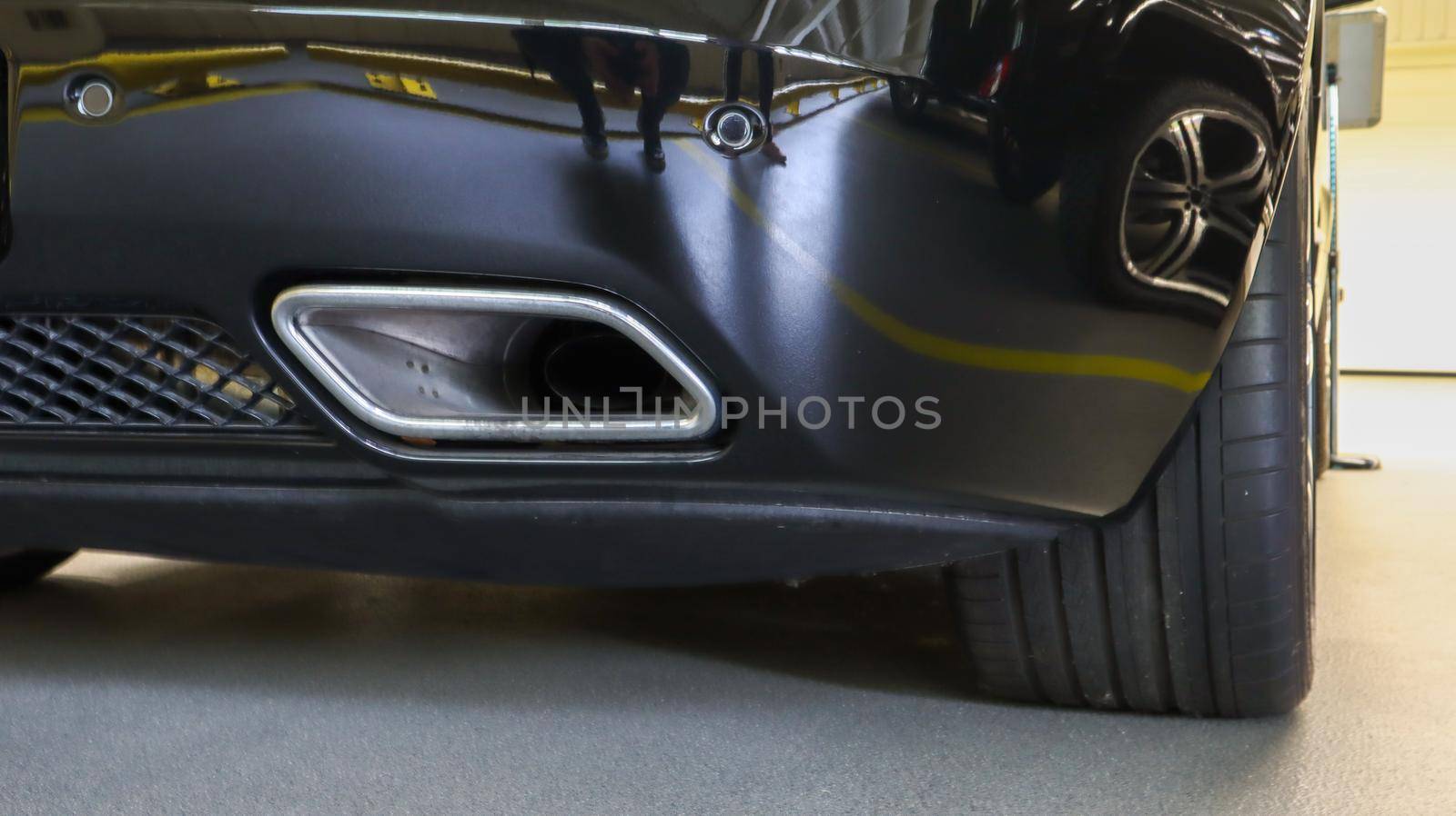 Square tailpipe at the rear right side of a black sports car. Very low plan. The rear bumper, wheel and tailpipe of the packed vehicle are smoke- and gas-free