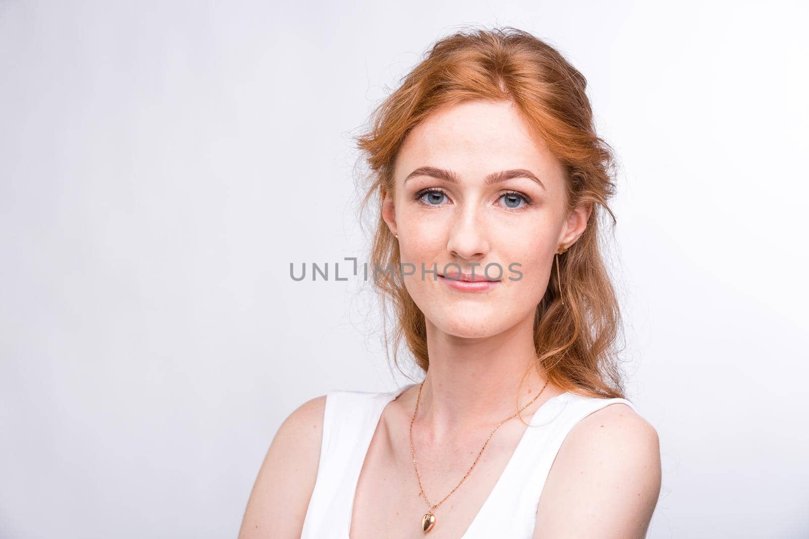 Portrait of a beautiful young woman of European, Caucasian nationality with long red hair and freckles on her face posing on a white background in the studio. Close-up student girl in a white blouse.