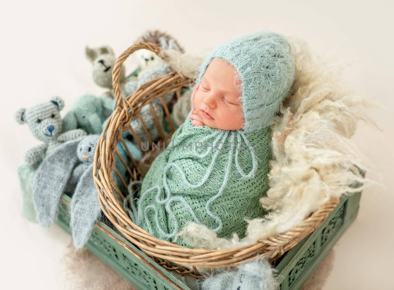 Cute newborn boy wrapped in a blanket sleep inside the basket with the toys