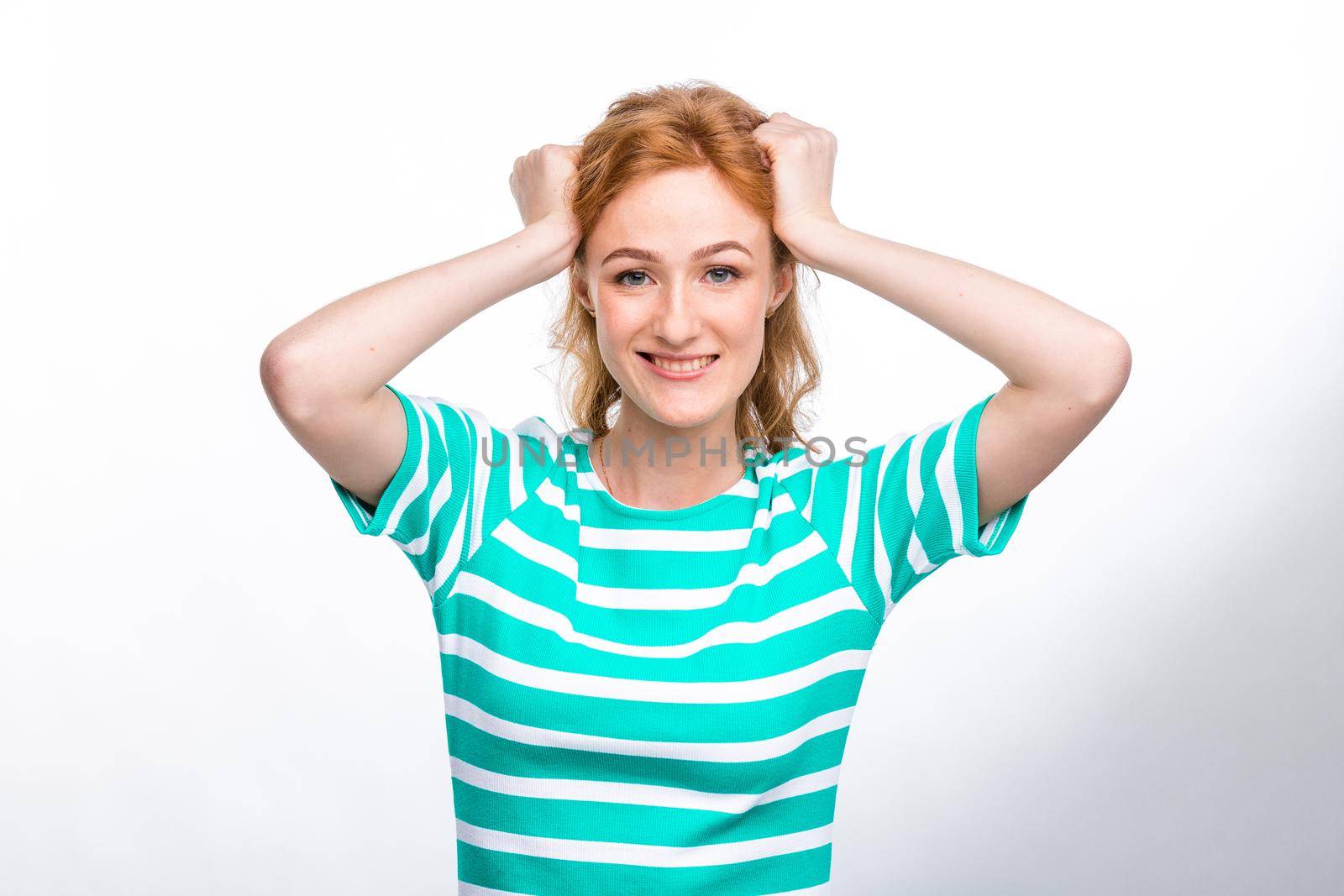 Close-up portrait of a young, beautiful woman with red curly hair in a summer dress with strips of blue in the studio on a gray background. Theme of summer vacation, tourism and summer clothes.