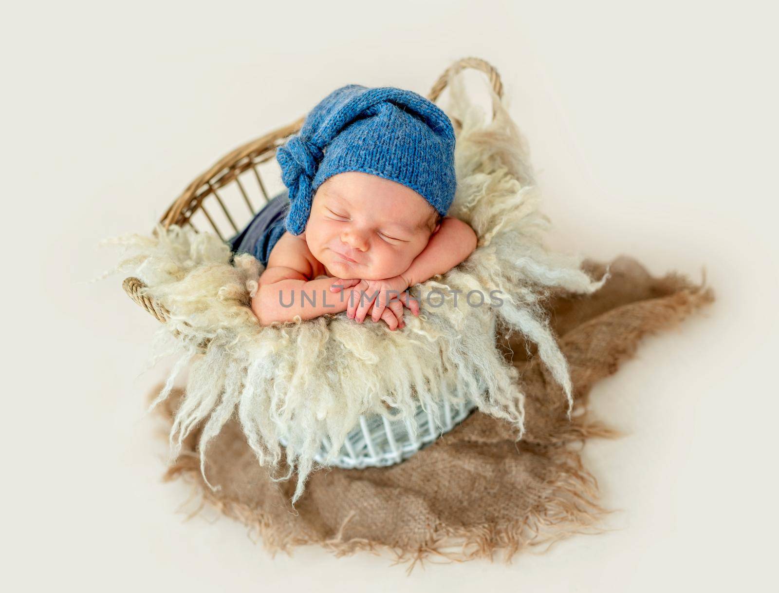 Cute newborn boy in a blue cap sleep inside the basket with the toys