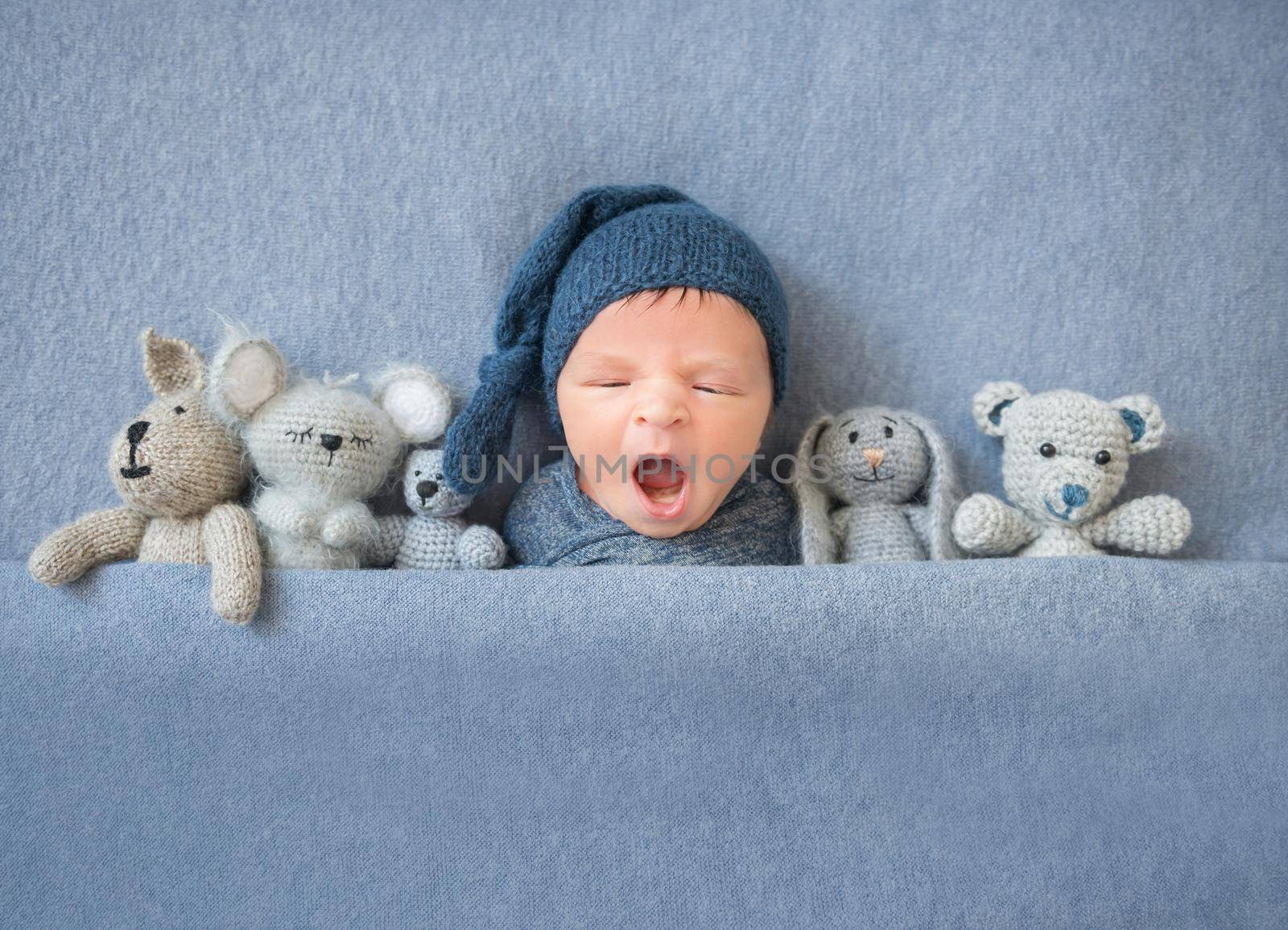 Newborn baby boy lying between plush toys, top view. Little newborn kid yawning