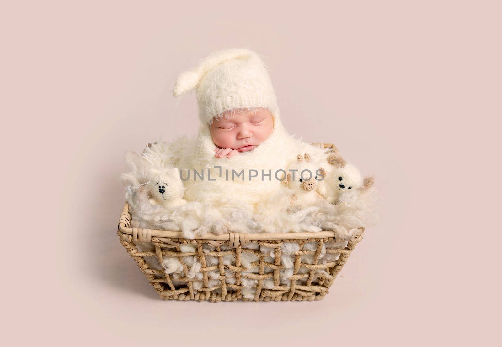 Charming little newborn baby with chubby cheeks sleeping happily in basket with soft toys. Babby wrapped in soft knitted scarf