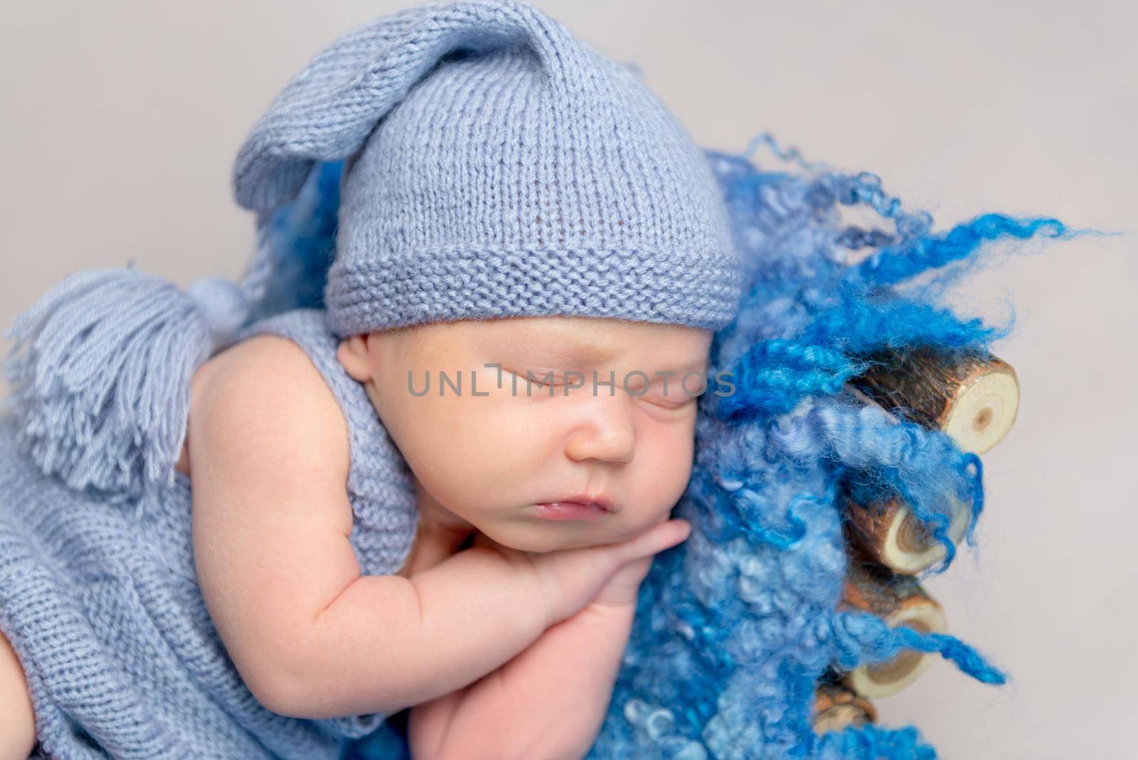 Cute baby dressed in knitted yellow costume sleeping on small wooden crib with one leg on the floor