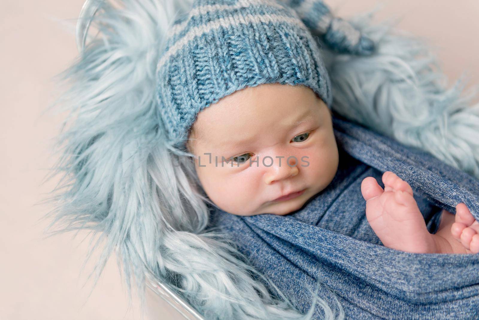 Newborn baby lying in trough with blue fluffy blanket. Little newborn baby boy wrapped in blue blanket and wearing in blue bonnet