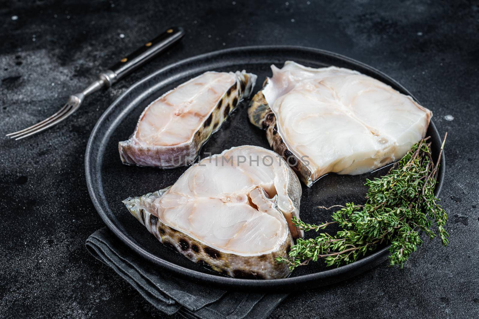 Fresh Raw wolffish o wolf fish Steak on a plate. Black background. Top view.