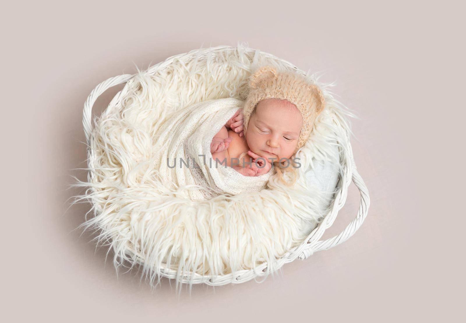 Newborn baby in funny bonnet napping in basket by tan4ikk1