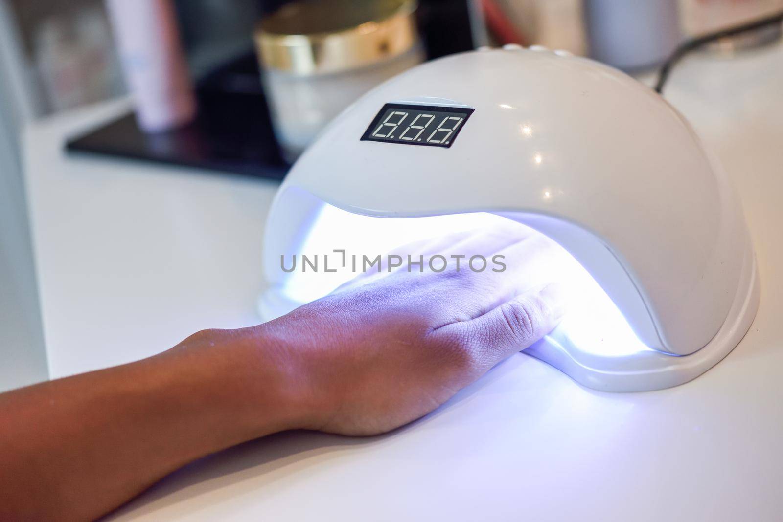 Manicured nails in UV lamp. Small nail art and manicure business. Hands of woman in a wellnes salon