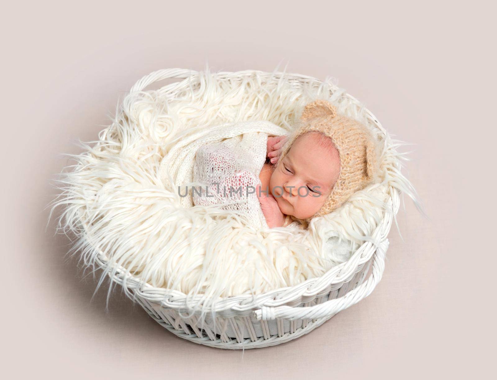 Adorable newborn baby napping in white round basket, top view. Little newborn baby in funny bonnet with ears