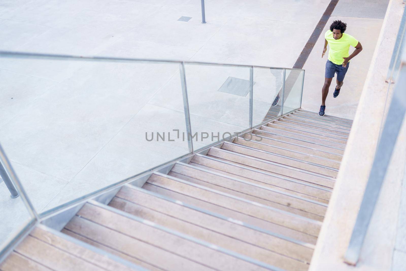 Black man running upstairs outdoors. Young male exercising. by javiindy