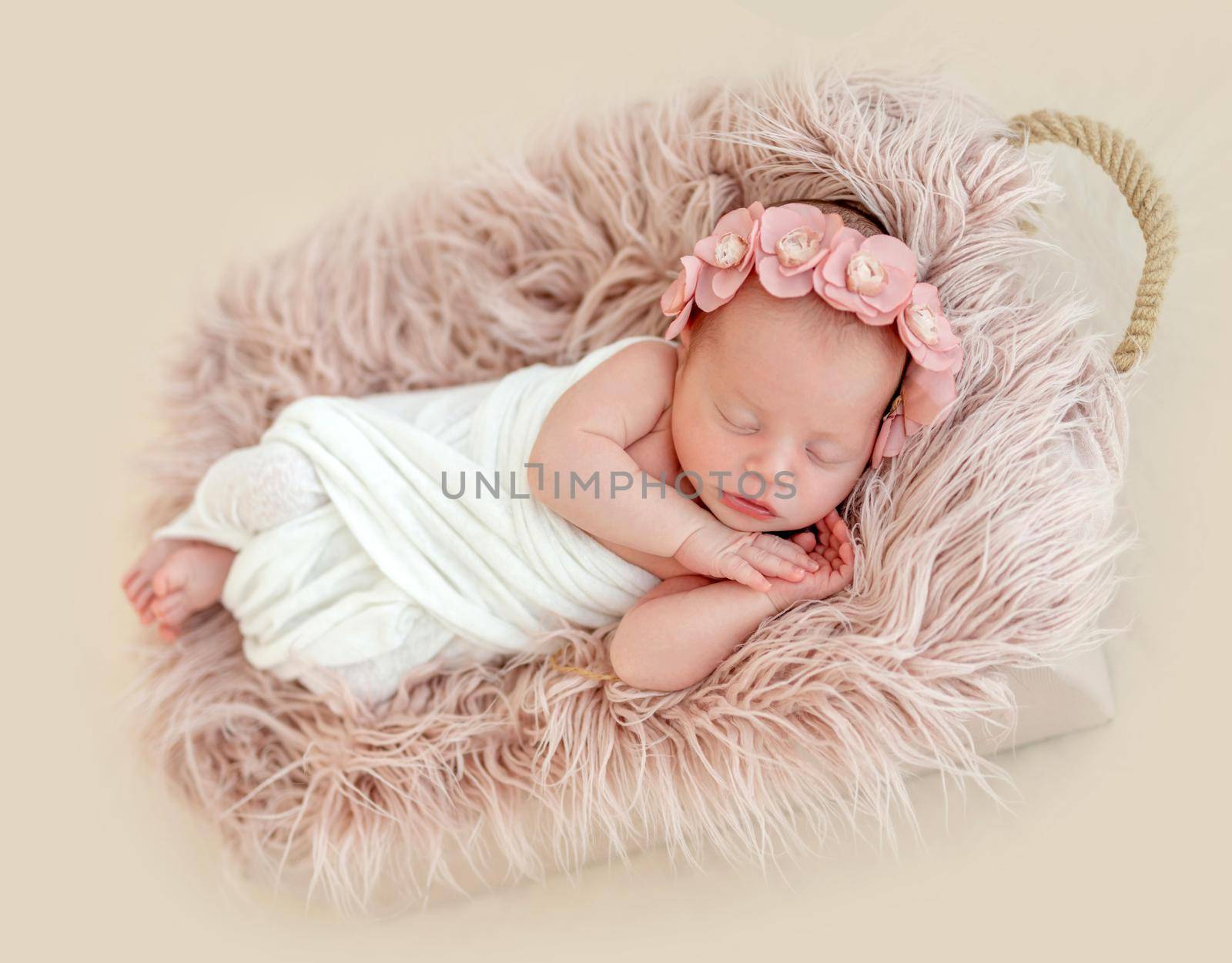 Beatiful newborn girl in floral headband, lying in sleeping basket in blanket