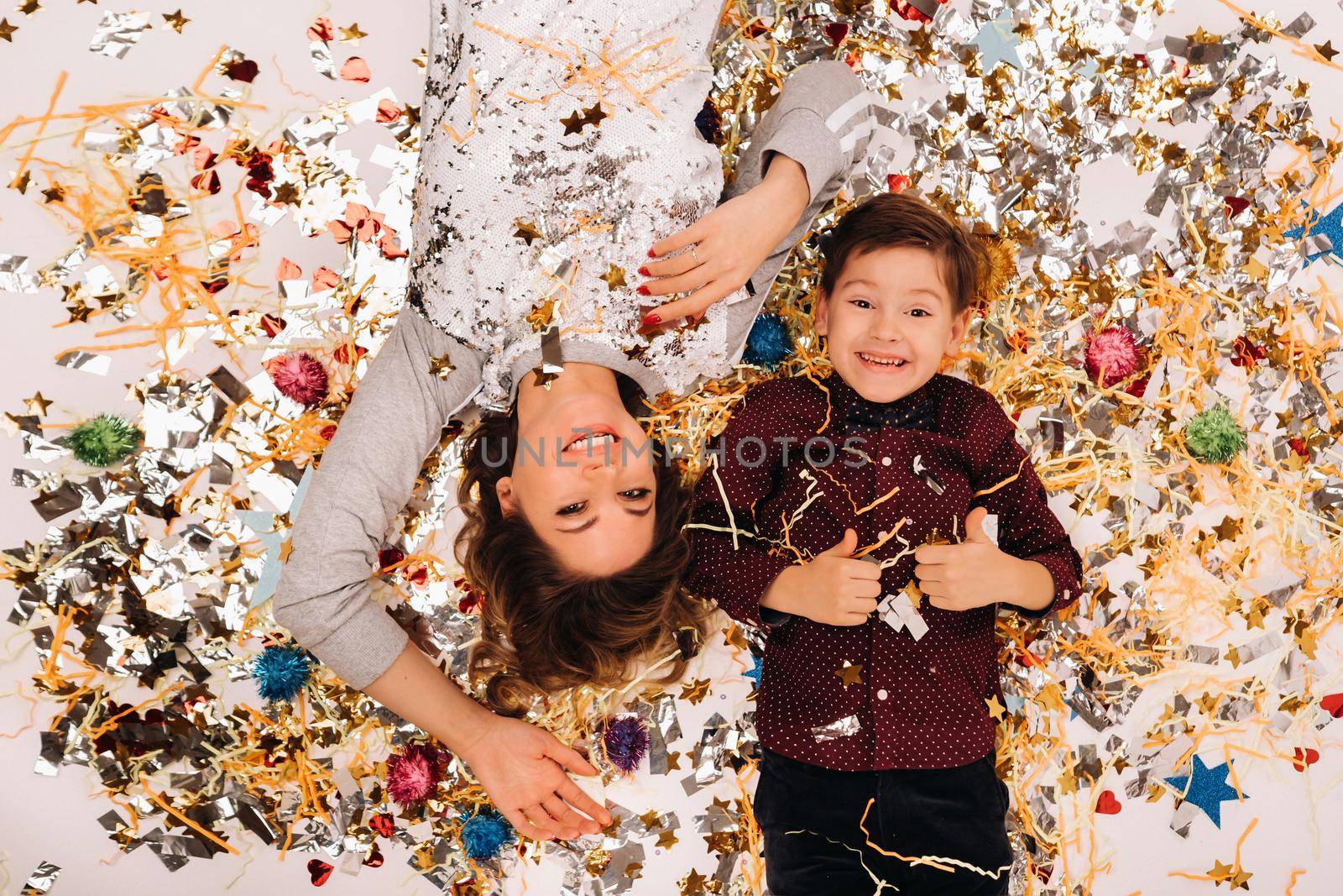 mother and son lie on the floor in confetti on a white background. A woman and a boy in confetti on a white background.