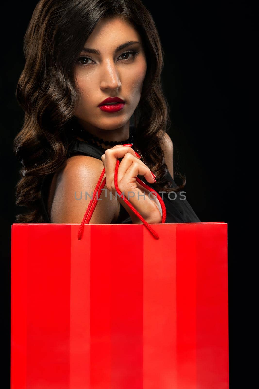 Black friday sale concept. Shopping woman holding red bag isolated on dark background in holiday by MikeOrlov