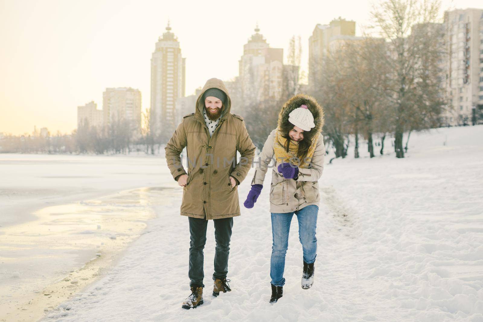 Young Caucasian people in love heterosexual couple have a date in winter near a frozen lake. Active holiday holiday Valentine's Day, playing snowballs and playing joy.