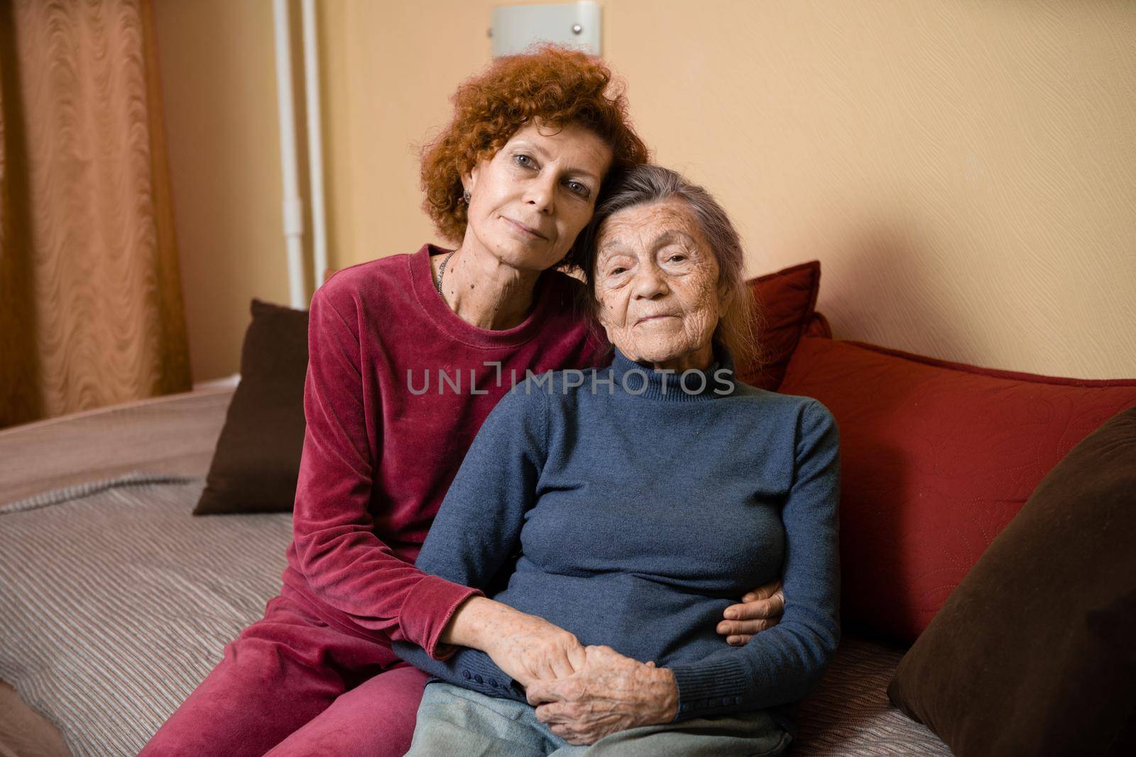 Adult daughter takes care of elderly mother suffering from dementia, old woman ninety years age gray hair and wrinkles on face and sweet kind smile, family idyll caring for elderly, hug each other.