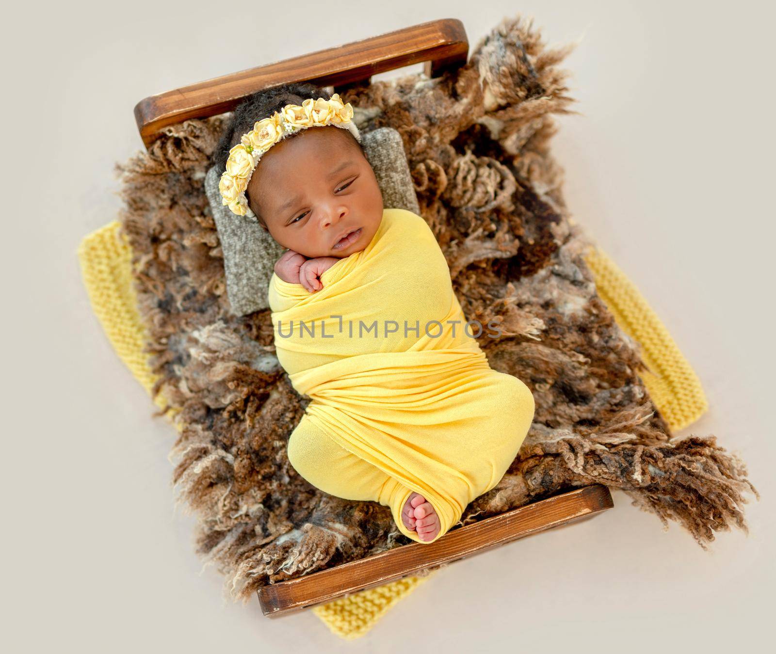 Pretty African newborn baby swaddled in yellow diaper lying in cradle