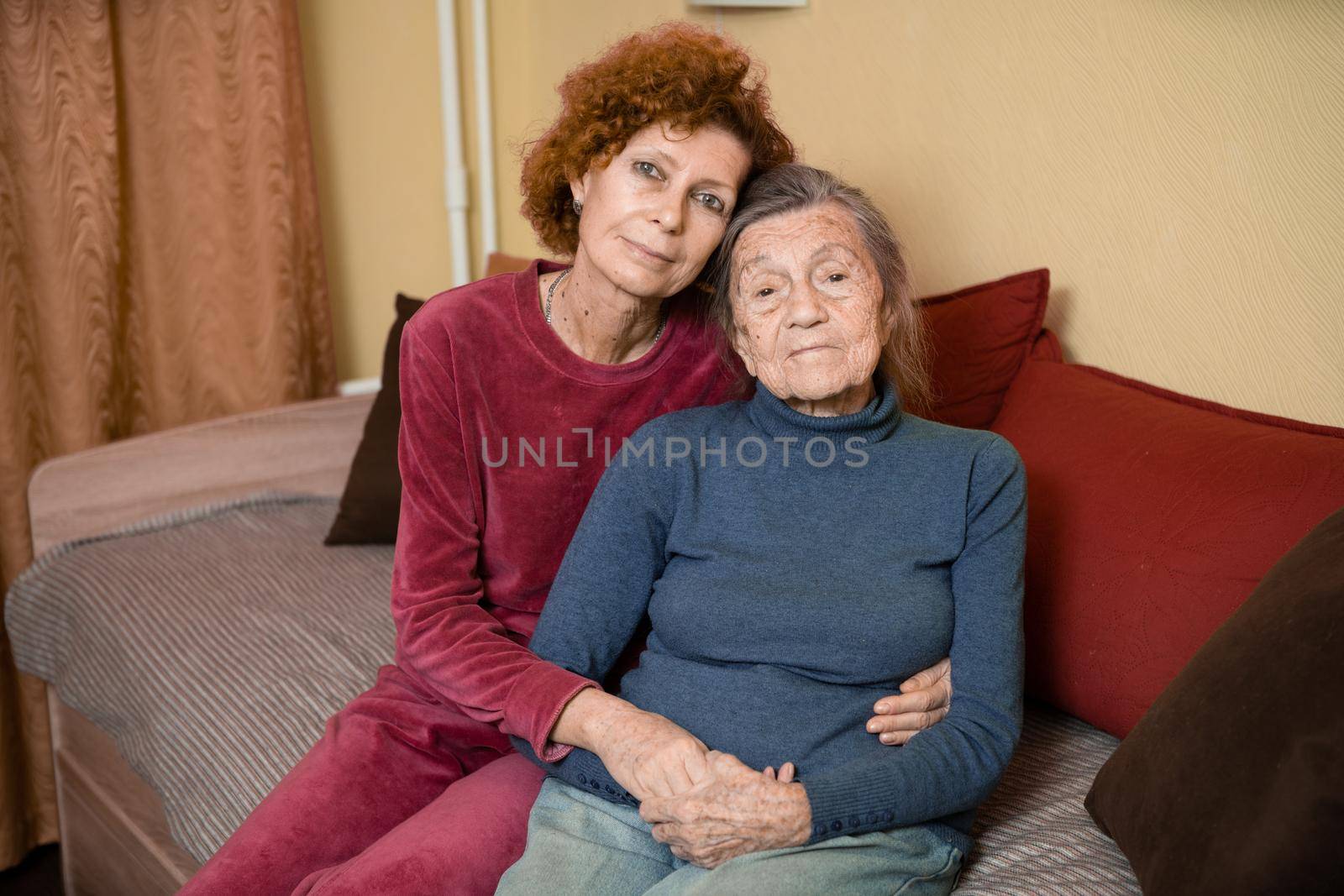 Elderly old cute woman with Alzheimer's very happy and smiling when eldest daughter hugs and takes care of her, at home on sofa. Theme aging and parenting, family relationships and social care oldest.