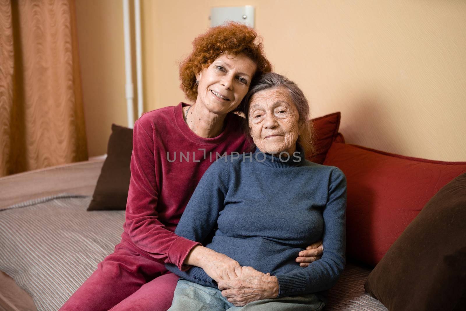 Elderly old cute woman with Alzheimer's very happy and smiling when eldest daughter hugs and takes care of her, at home on sofa. Theme aging and parenting, family relationships and social care oldest by Tomashevska