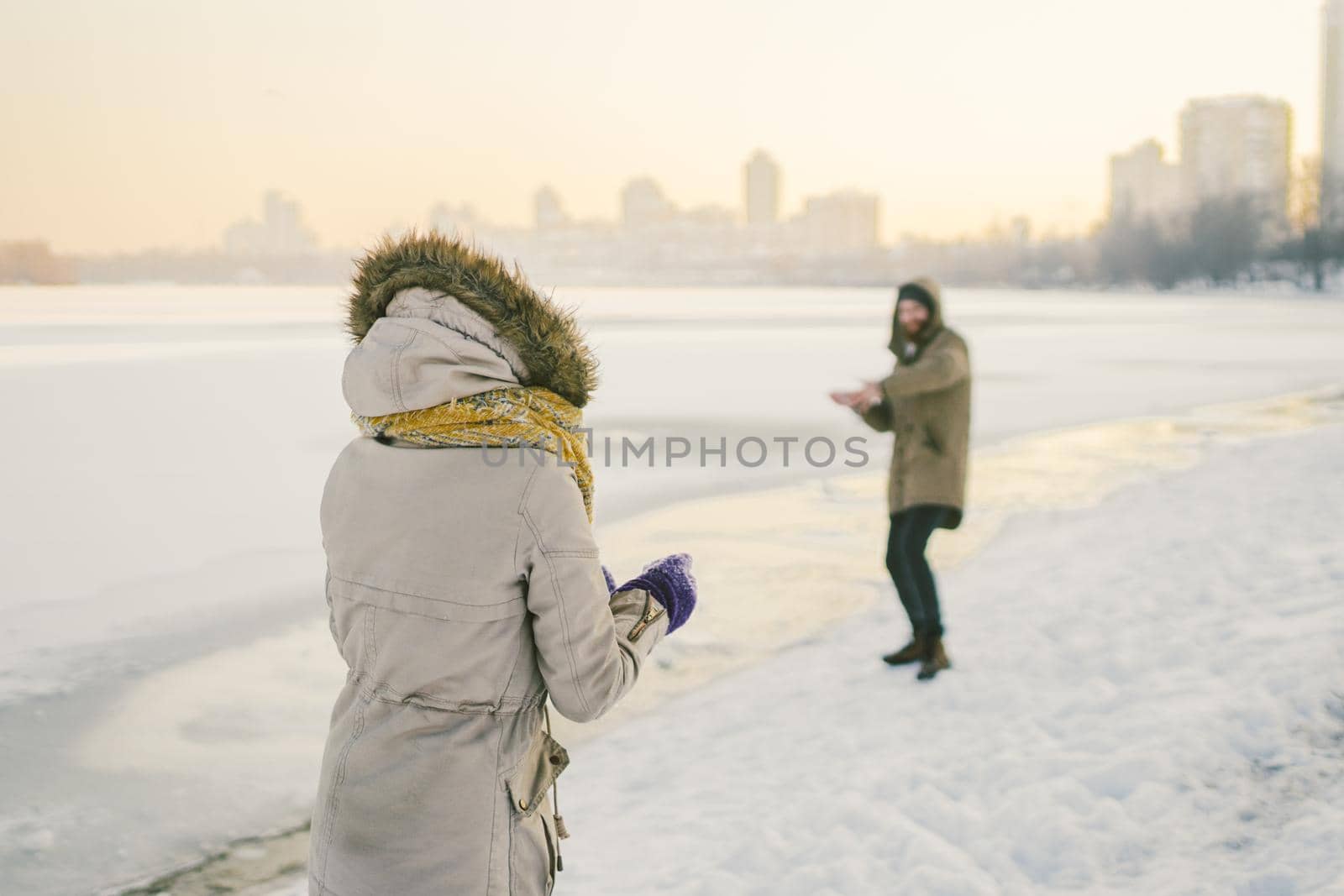 Young Caucasian people in love heterosexual couple have a date in winter near a frozen lake. Active holiday holiday Valentine's Day, playing snowballs and playing joy by Tomashevska