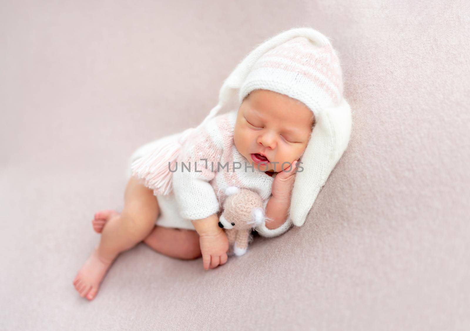 Cute newborn baby in funny hat slepping with toy