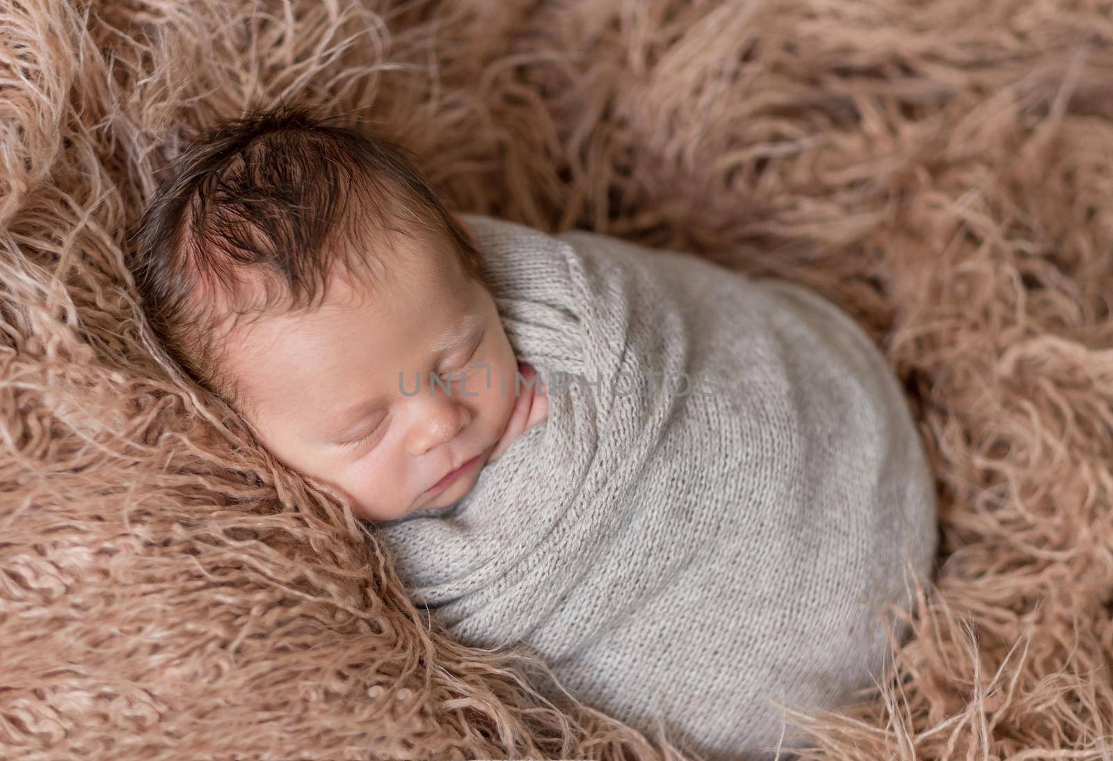 Little cute baby covered with gray knitted blanket sweetly sleeping on the soft light brown bedcover