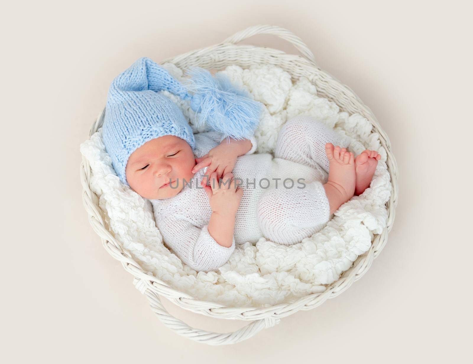 Cute newborn in knitted suit and hat lying in white basket