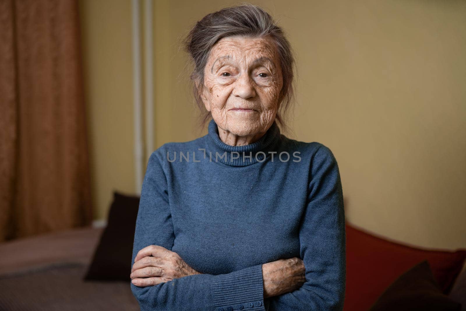 90 year old cute elderly woman with gray hair and wrinkles face, wearing sweater, portrait large, smiling and looking joyfully, background of room. Theme long-liver and aging, old people in good mood.