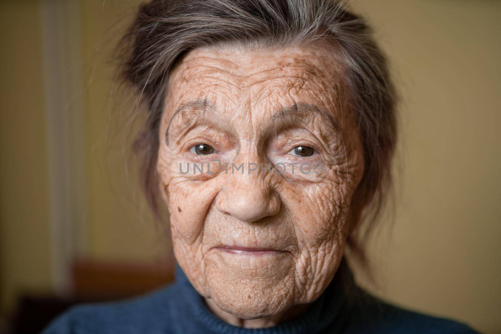 90 year old cute elderly woman with gray hair and wrinkles face, wearing sweater, portrait large, smiling and looking joyfully, background of room. Theme long-liver and aging, old people in good mood by Tomashevska