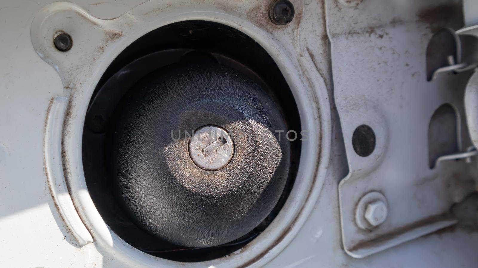 Fuel cap of a white sports car. Close the gas tank cap. The fuel tank is open. The fuel filler door is open and the fuel filler flap is closed. The exterior of the car with the filler door open
