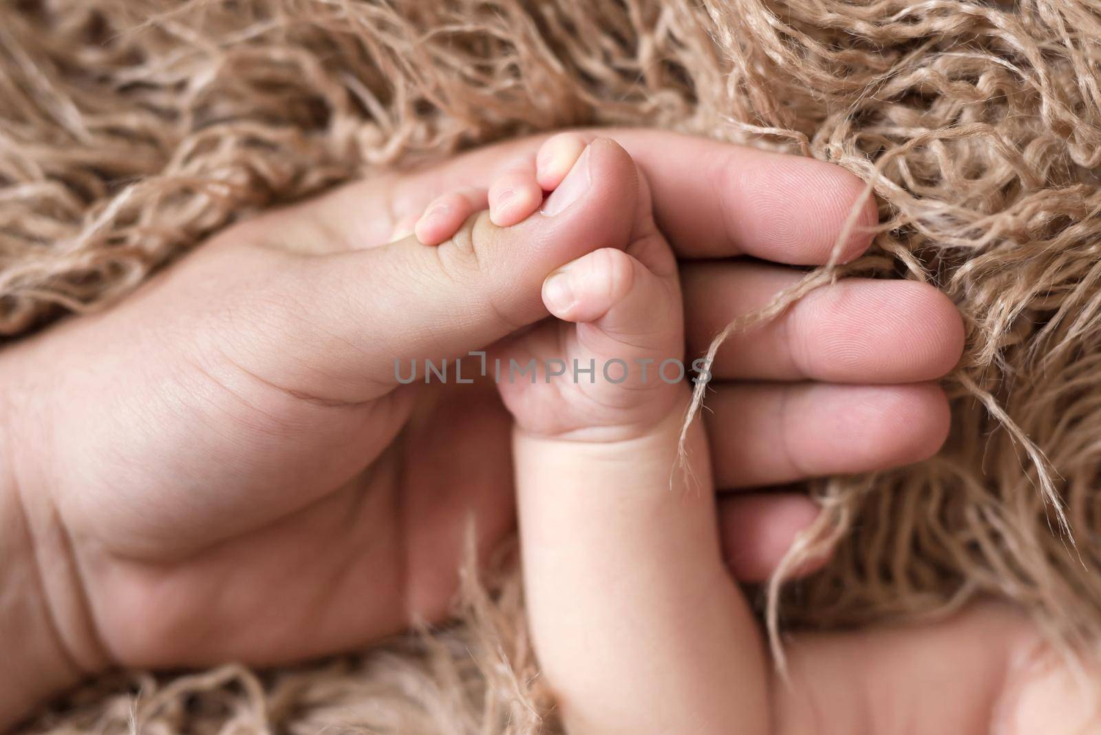 Parent holding little baby's hand on the light brown bedcover background