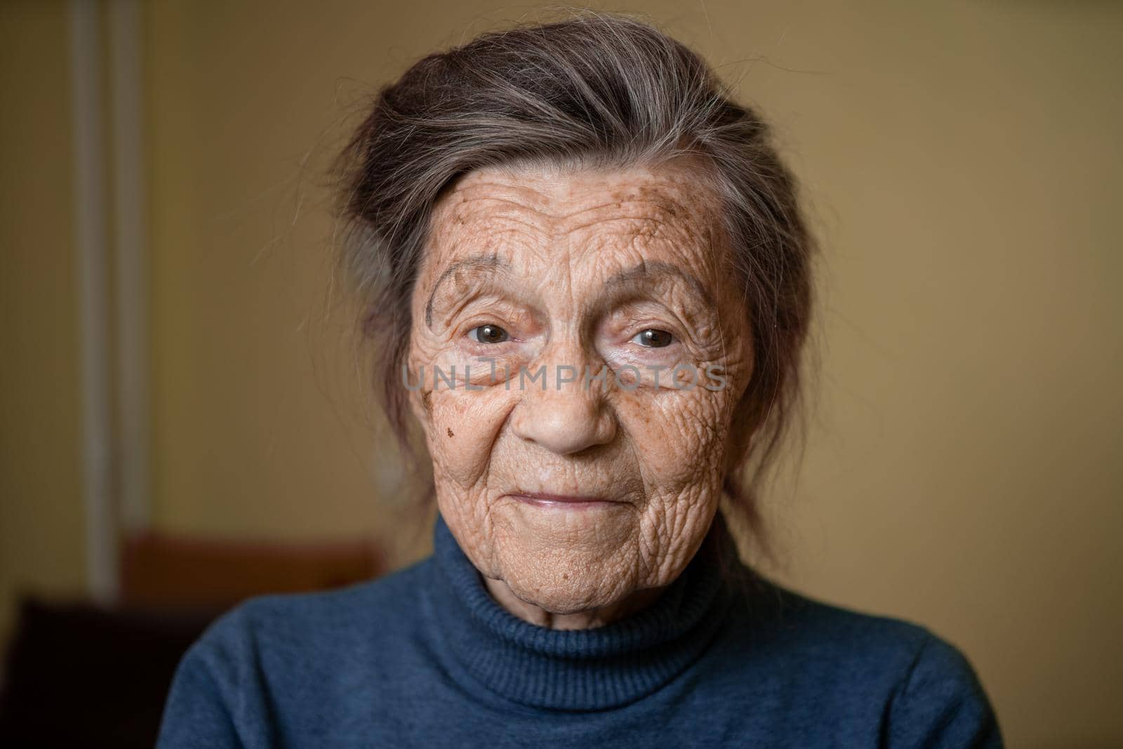 Older cute woman of ninety years old Caucasian with gray hair and wrinkled face looks at camera, cute kind look and smiles.Mature grandmother retired long-liver, theme emotion and mood of old people.